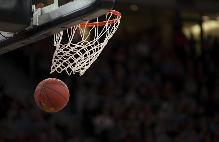 NBA篮球比赛中，运动员腾空而起暴力扣篮，肌肉线条分明，球馆内灯光聚焦，观众席沸腾，展现篮球运动的暴力美学